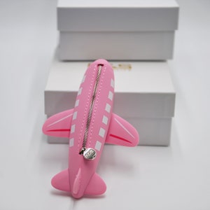 May include: Pink airplane-shaped zippered pouch with white squares and a silver zipper pull.