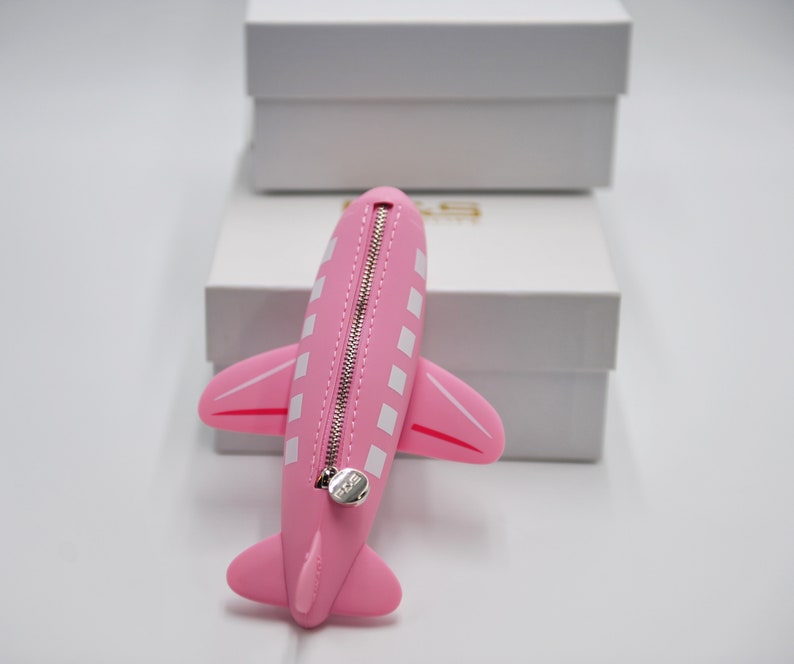 May include: Pink airplane-shaped zippered pouch with white squares and a silver zipper pull.
