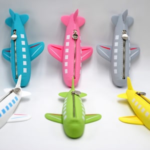 May include: Five airplane-shaped zippered pouches in different colors: blue, pink, gray, white, and yellow. Each pouch has a zipper closure and white squares along the side.