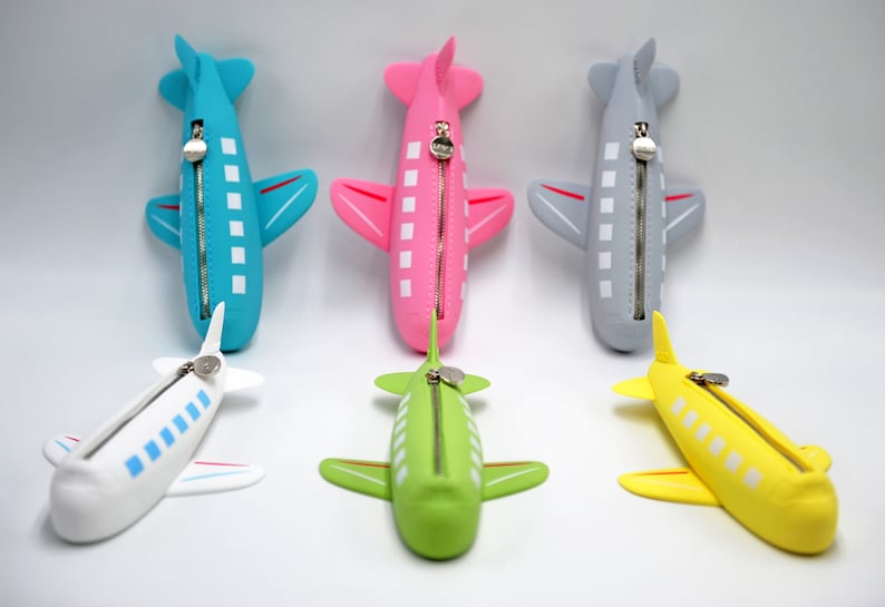 May include: Five airplane-shaped zippered pouches in different colors: blue, pink, gray, white, and yellow. Each pouch has a zipper closure and white squares along the side.