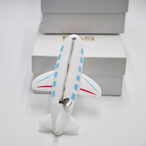 May include: White airplane-shaped zippered pouch with blue and red accents. The pouch is lying on a white surface.