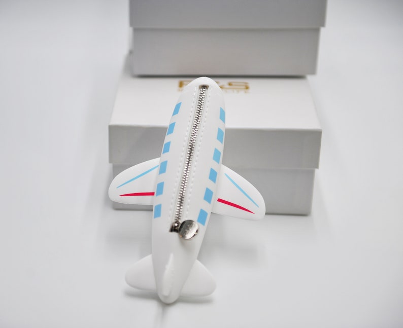 May include: White airplane-shaped zippered pouch with blue and red accents. The pouch is lying on a white surface.