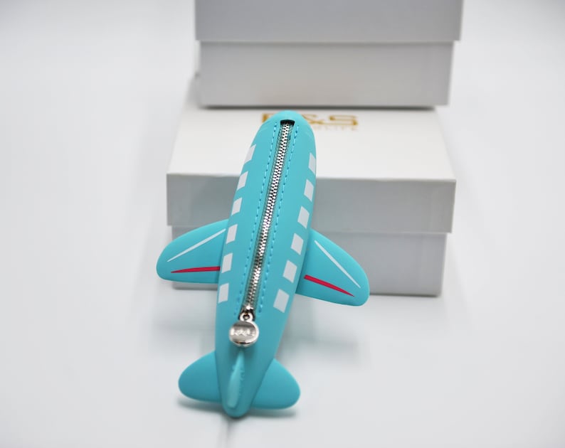 May include: A blue airplane-shaped zippered pouch with white and red details. The zipper is silver and the pouch is made of a soft, pliable material.
