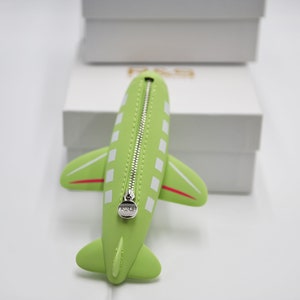May include: A green airplane-shaped zippered pouch with white squares and a red stripe. The zipper pull has a silver charm with the word "F.R.S." on it.