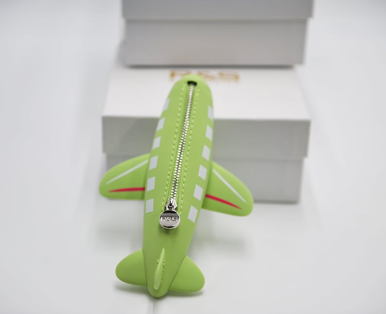 May include: A green airplane-shaped zippered pouch with white squares and a red stripe. The zipper pull has a silver charm with the word "F.R.S." on it.