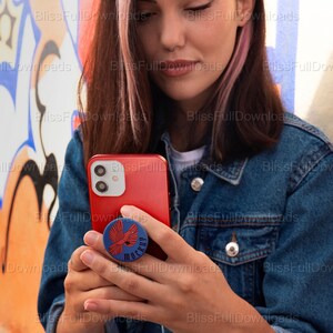 May include: A person holding a red iPhone with a blue and red pop socket featuring a bird design and the word "MOCKUP".