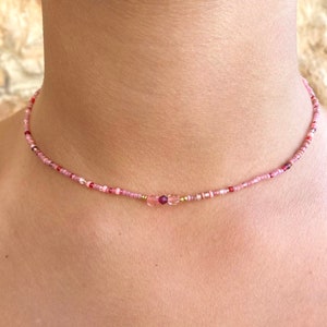 May include: A delicate pink and gold beaded choker necklace with two larger pink crystal beads in the center.