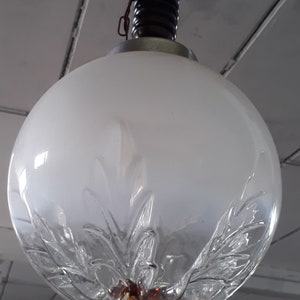 May include: A vintage globe pendant light with a frosted glass shade. The lower portion of the shade features a clear, leaf-like design. The light fixture has a dark brown, ribbed top and a metal ring.