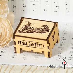 Könnte beinhalten: Eine hellbraune Holz-Spieluhr mit der Gravur "FINAL FANTASY X" auf der Vorder- und Oberseite. Die Oberseite zeigt eine detaillierte Illustration. Die Box steht auf Notenblättern. Das Logo "Sinfonia Italiana" ist sichtbar.