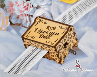 May include: Wooden music box with a hand-crank and a paper music sheet that reads "I Love You Dad". The box is decorated with hearts and swirls.