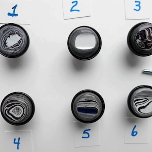 May include: Six round, black and white patterned knobs with a silver screw. The knobs are numbered 1 through 6.