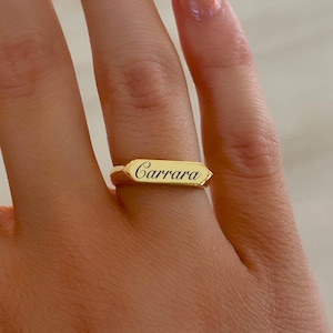 Puede incluir: Un anillo de oro con el nombre "Carrara" grabado.