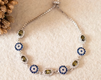 Pode incluir: Uma pulseira de prata com um design de corrente e vários amuletos de olho turco azuis e verdes. Os amuletos são adornados com pedras transparentes e azuis.