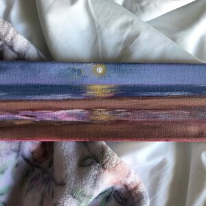 Puede incluir: Una pintura de un paisaje marítimo con un cielo morado, un océano azul oscuro y una playa de arena. El sol se está poniendo en la distancia, proyectando un brillo dorado sobre el agua.