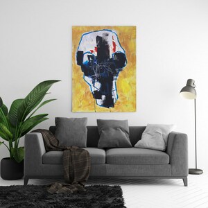 May include: Abstract art piece with a yellow background and a central figure in black, white, and red. The artwork is framed with a blue outline and hangs above a gray sofa with pillows and a plaid throw. A floor lamp and a potted plant are also in the room.