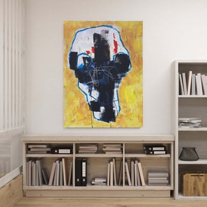 May include: Abstract painting on canvas with a yellow background and a central black and white form outlined in blue. Red accents and linear details add visual interest. The artwork is displayed above a wooden bookshelf.