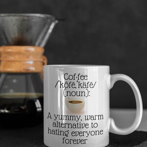May include: White coffee mug with the text "Coffee /'k&ocirc;fē, k&auml;fe/ (noun): A yummy, warm alternative to hating everyone forever." A glass coffee maker is in the background.