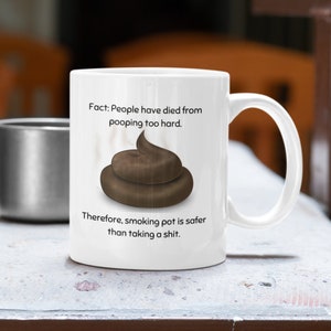 May include: White ceramic mug with a humorous design. The mug features a brown illustration of a pile of poop and the text: "Fact: People have died from pooping too hard. Therefore, smoking pot is safer than taking a shit."