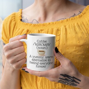 May include: A white ceramic coffee mug with the text "Coffee /'kōfē, kāfē/ (noun): A yummy, warm alternative to hating everyone forever." The mug has a handle and a small coffee cup graphic.