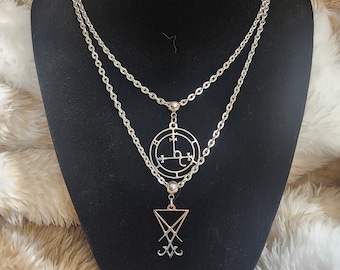 May include: A silver chain necklace with two pendants. The top pendant is a circle with a symbol inside. The bottom pendant is a triangle with a symbol inside.