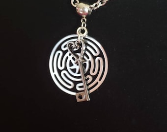 May include: A silver necklace with a circular pendant featuring a key and a heart inside a maze design.