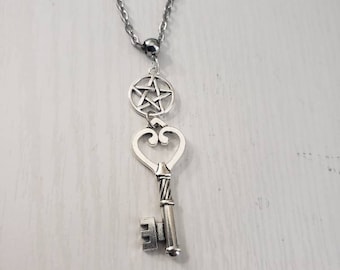 May include: A silver necklace with a key pendant and a pentagram charm. The key has a heart-shaped bow at the top and a detailed design on the shaft. The pentagram charm is circular and has a five-pointed star inside.