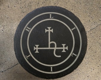 May include: Round black slate coaster with a white graphic design. The design features a circular border with the letters H, L, I, and T, and a central symbol with cross-like elements and a curved line. The coaster is on a textured surface.