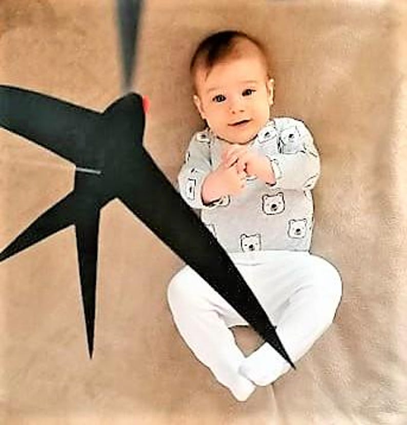 A baby lying beneath the hanging swallows mobile, calmly observing the gentle movement of the shapes above.