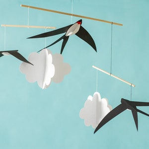 Black and white paper swallows hanging in front of a light blue background, part of a calm Montessori-inspired baby mobile