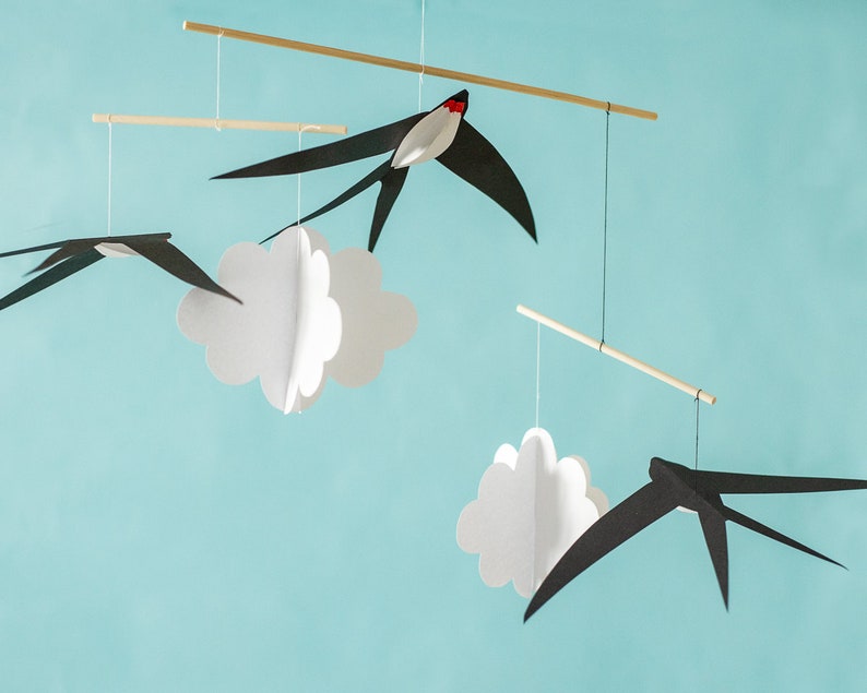 Black and white paper swallows hanging in front of a light blue background, part of a calm Montessori-inspired baby mobile