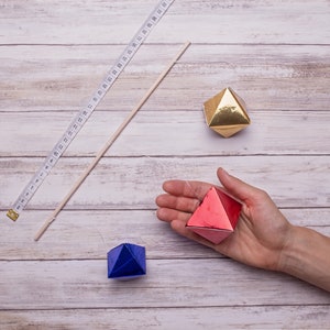 The measurements of the DIY Montessori Octahedron baby mobile, a tape and one of the octahedron is held in hand for scale