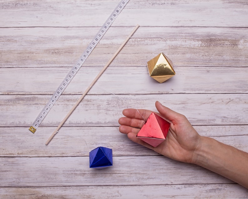 The measurements of the DIY Montessori Octahedron baby mobile, a tape and one of the octahedron is held in hand for scale