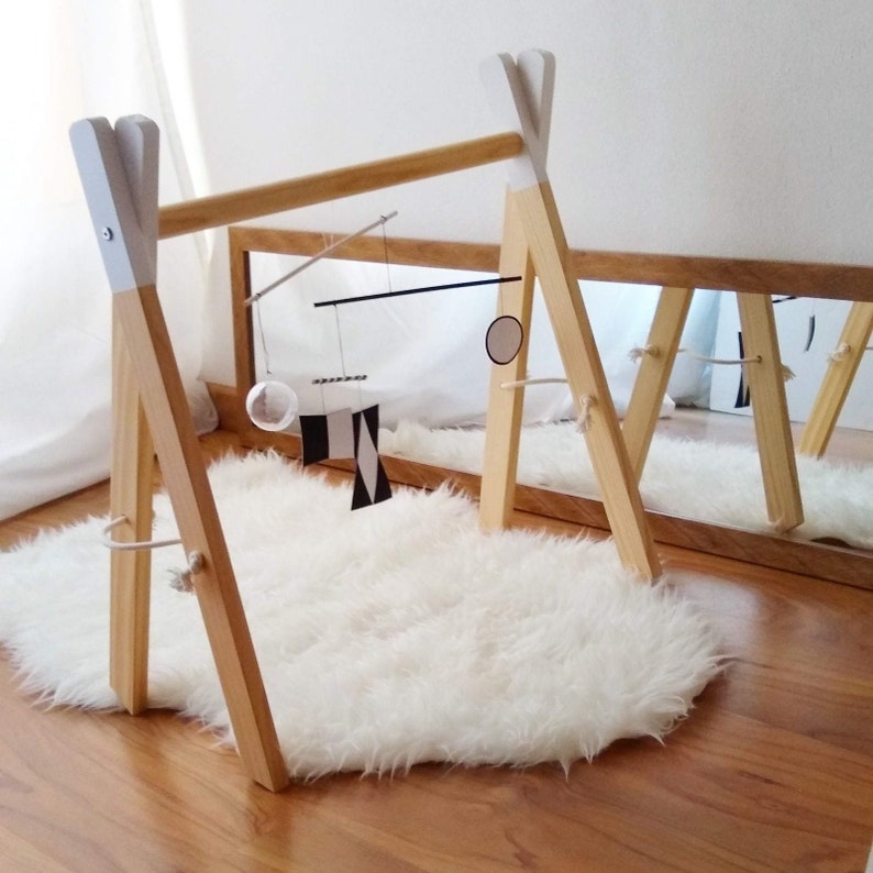The Montessori Munari mobile hanging on a mobile stand. There's a soft fake sheepskin under it and a mirror on the side.