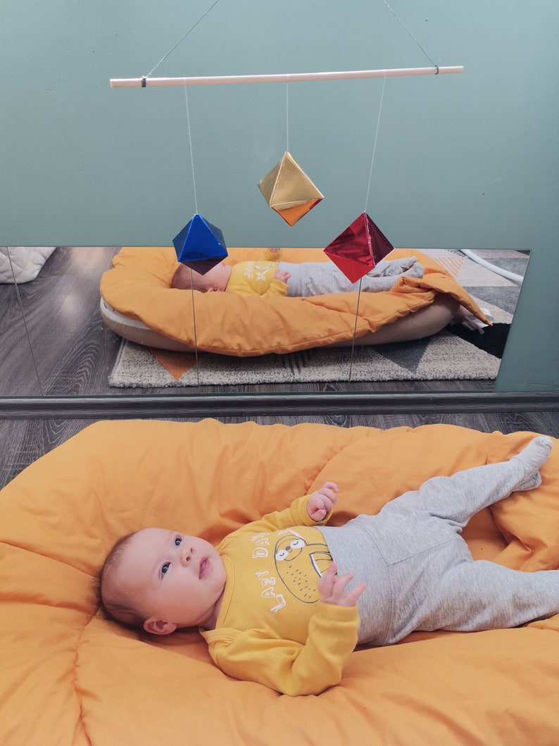 A baby girl in a room, looking at the DIY Montessori Octahedron baby mobile