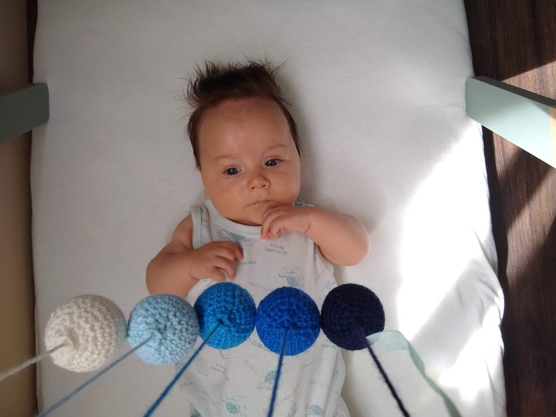 A baby boy is observing the Crocheted Gobbi mobile