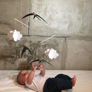 The DIY Montessori Swallows Mobile, hanging above a baby who stretches his arms towards the lowers bird