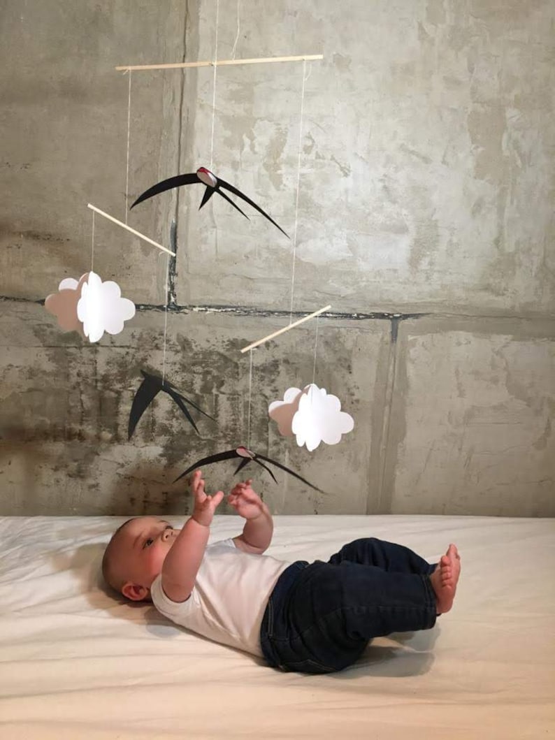 The DIY Montessori Swallows Mobile, hanging above a baby who stretches his arms towards the lowers bird