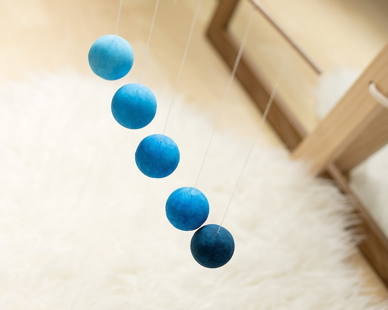 The blue version of the DIY Montessori Gobbi mobile kit for newborn visual development, is hanging on a mobile hanger.
