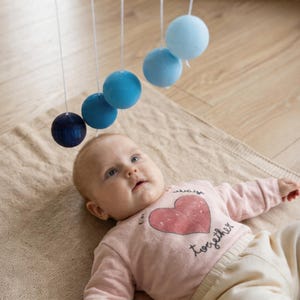 A baby girl is looking at the DIY Montessori Gobbi mobile kit for newborn visual development