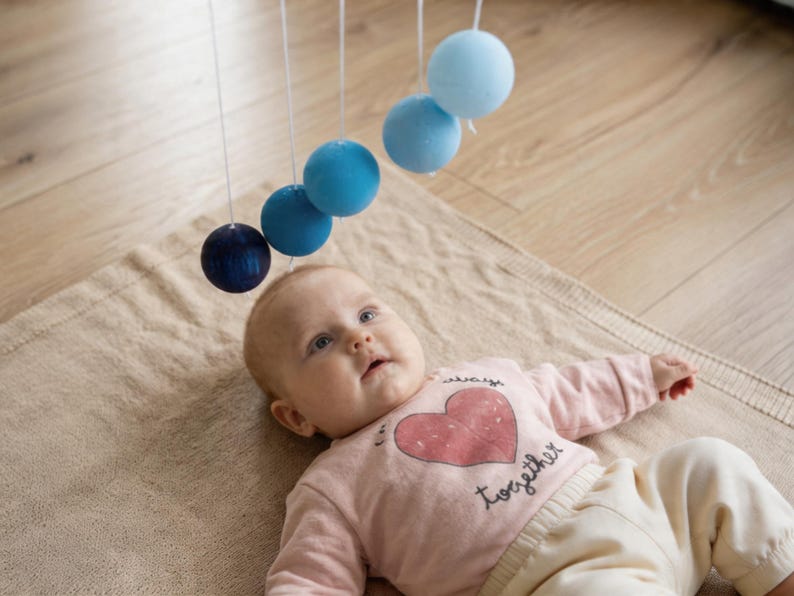 A baby girl is looking at the DIY Montessori Gobbi mobile kit for newborn visual development