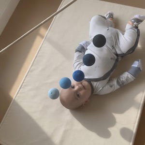 A baby boy in his cot is looking at the DIY Montessori Gobbi mobile kit for newborn visual development