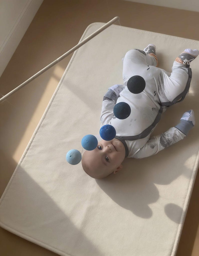 A baby boy in his cot is looking at the DIY Montessori Gobbi mobile kit for newborn visual development