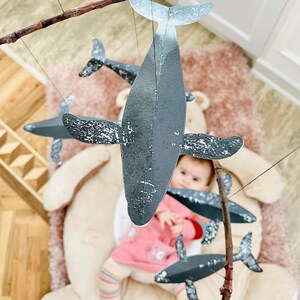 A baby girl is looking at the DIY Montessori Whale Mobile