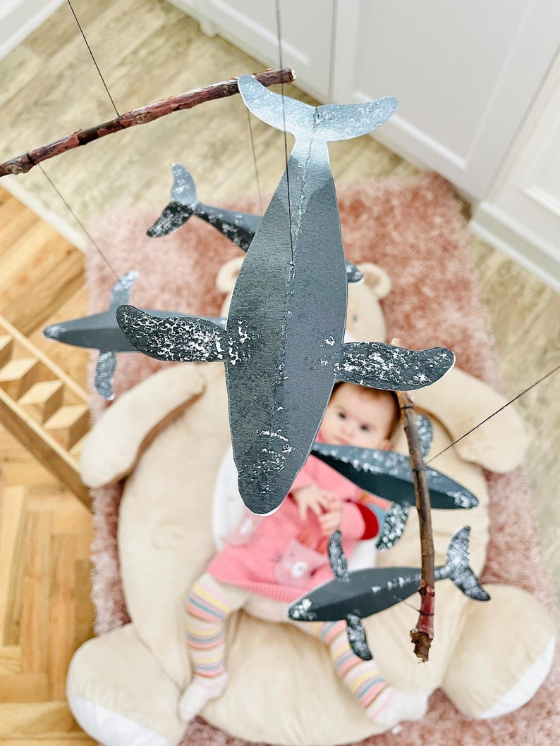 A baby girl is looking at the DIY Montessori Whale Mobile