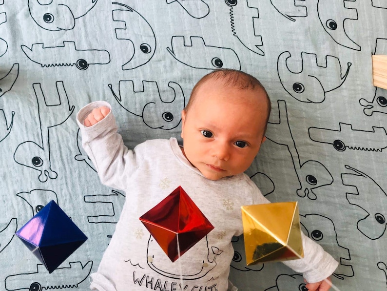 A baby boy is looking at the Montessori Octahedron mobile.