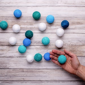 The balls of the DIY Montessori Gobbi mobile kit for newborn visual development, on a rustic wooden surface, with a hand holding a ball for scale
