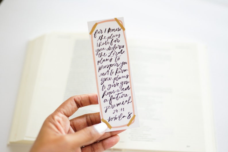 May include: A pink and gold bookmark with a handwritten quote from Jeremiah 29:11, "For I know the plans I hold for you, declares the Lord, plans to prosper you and not to harm you, plans to give you hope and a future."