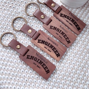 May include: Four wooden keychains with leather straps. Each keychain has a different type of engineer title: Chemical, Software, Aerospace, and Mechanical. Each title is engraved on the wood with the text "EST. 2024".