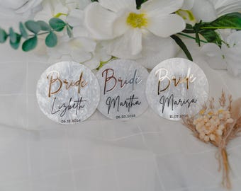 May include: Three circular white marbled acrylic discs featuring the word Bride in metallic script, followed by a name and a date. The first disc reads Lizbeth 06.19.2026, the second Martha 06.20.2026, and the third Marisa 11.07.2026 in black text.