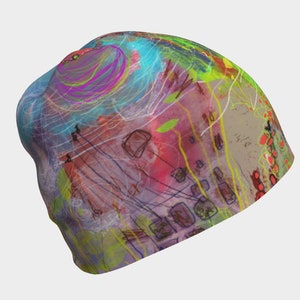 May include: A colourful beanie with abstract art in shades of pink, blue, green, yellow, and red. The beanie has a white background with black lines and shapes.